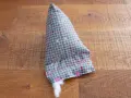 Un berlingot tissu gris à petits cœurs roses et blancs, en cours de rembourrage, est posé sur un parquet en bois.