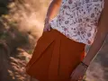 Jupe tulipe orange à plis, portée avec un haut fleuri. Le soleil couchant illumine la scène.