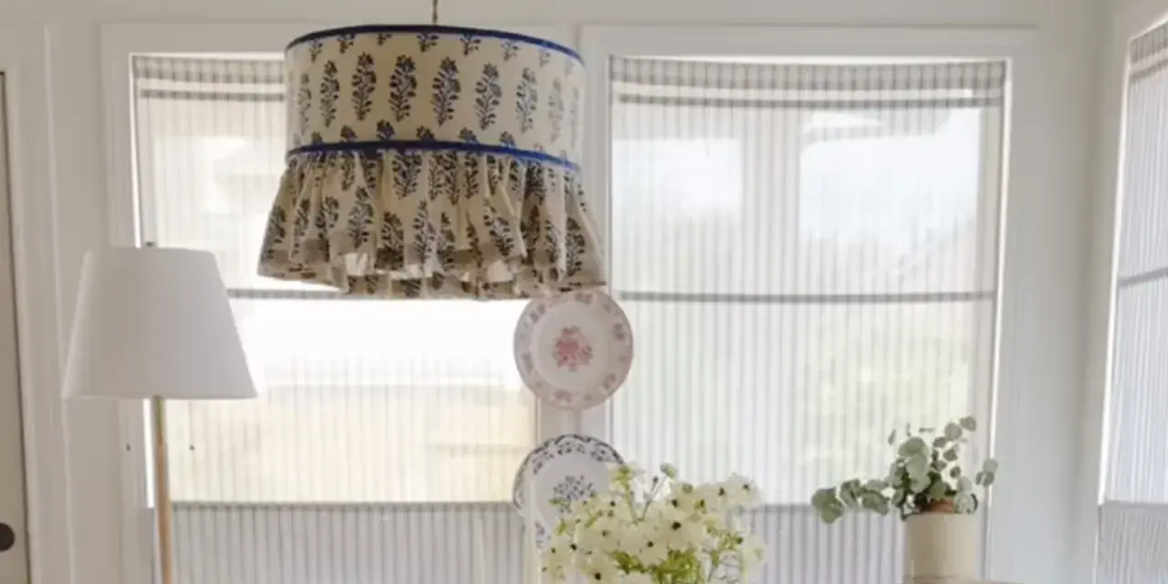 Un abat-jour suspendu avec un motif floral bleu et des volants, une excellente idée déco abat jour. Des assiettes décoratives et des fleurs complètent la scène.