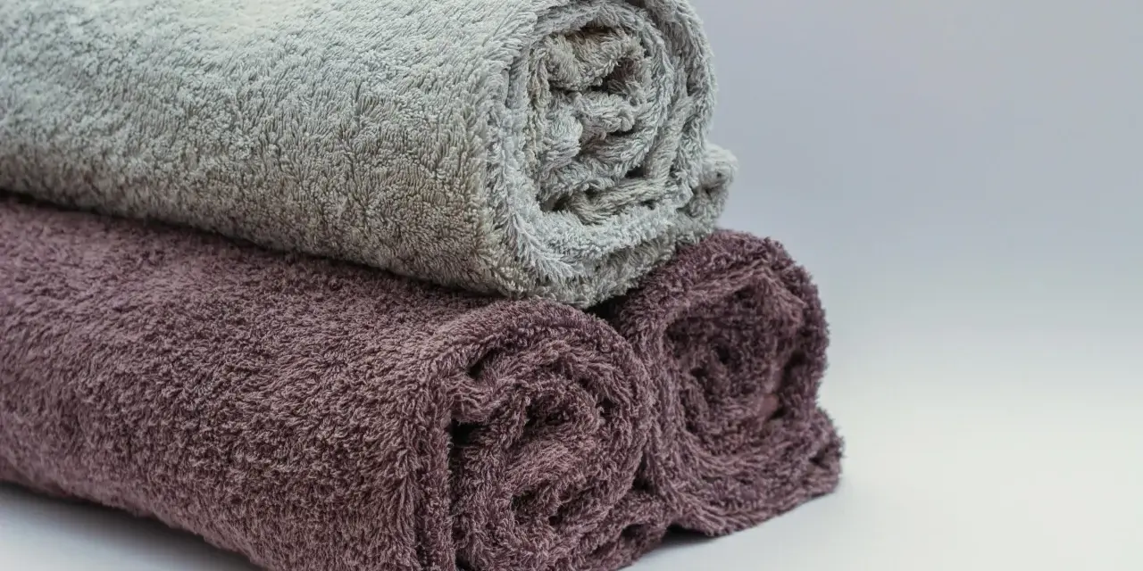 Trois serviettes de bain roulées, une grise et deux prune, prêtes à être cousues pour un projet de couture.