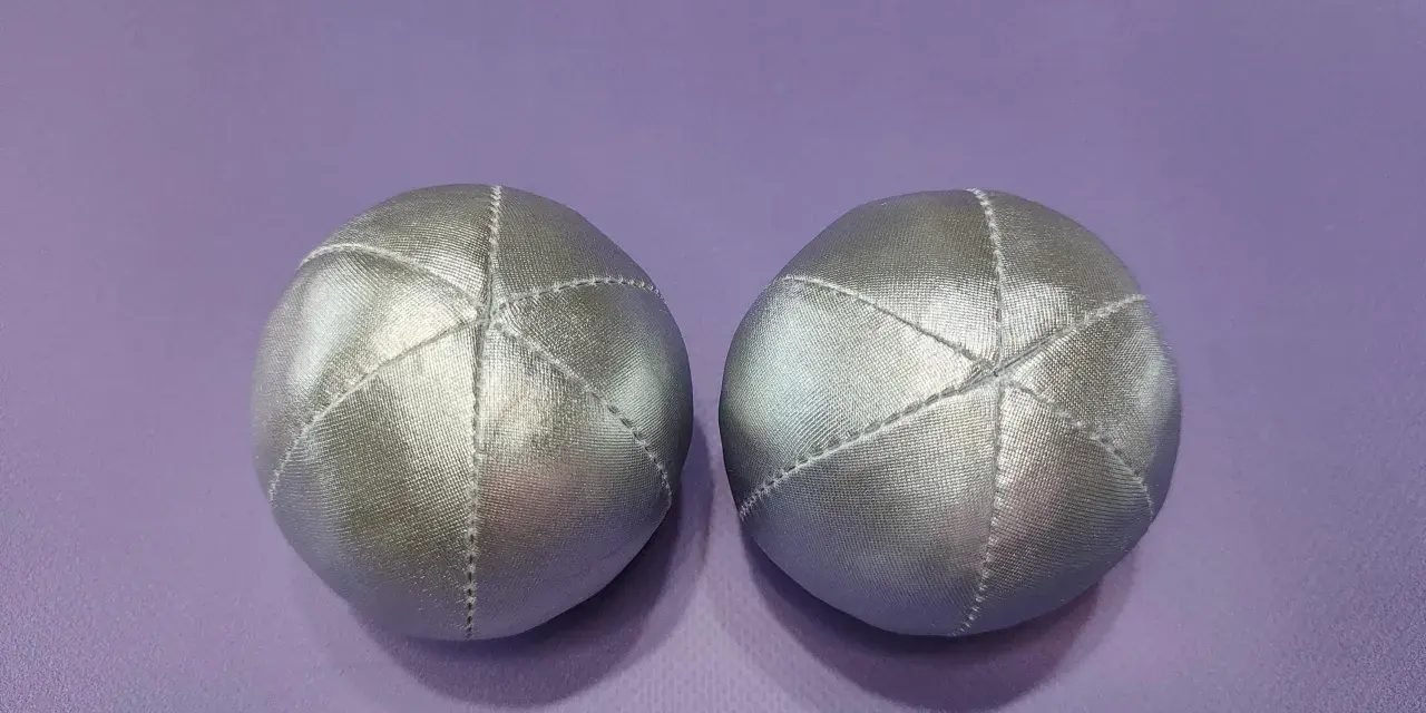Deux balles en tissu argenté, parfaites pour un **patron gratuit balle en tissu**. Elles sont posées sur un fond violet.