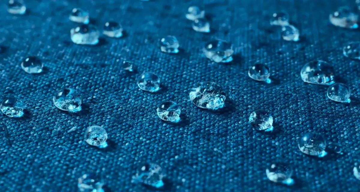 Gouttes d'eau perlant sur un tissu bleu, illustrant comment imperméabiliser un tissu naturellement.