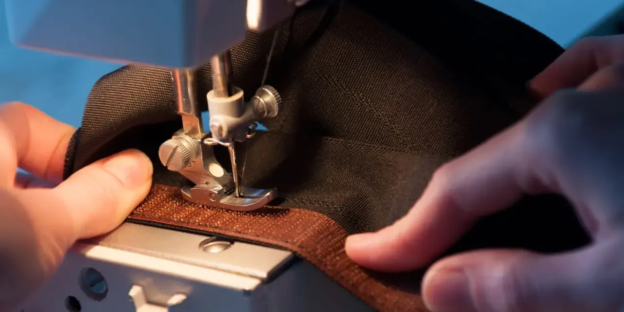 Mains habiles guidant un tissu noir sous une machine à coudre pour coudre du velcro marron.