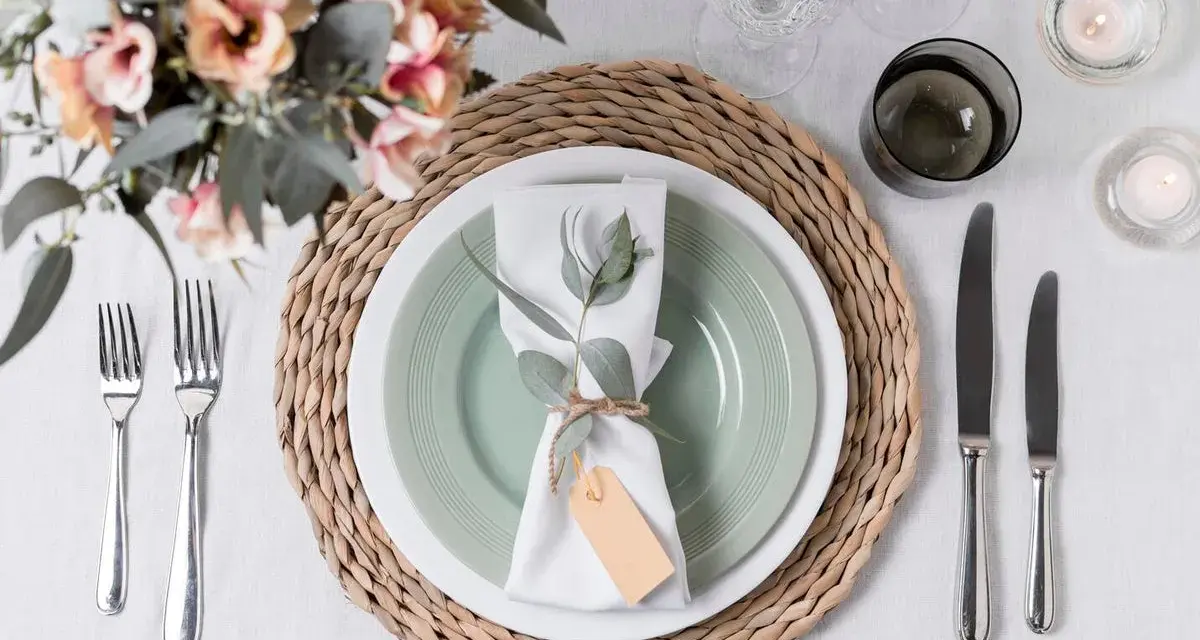 Une table dressée avec une assiette verte, une serviette blanche décorée d'une branche d'eucalyptus et d'une étiquette, le tout sur un rond de serviette fait maison.