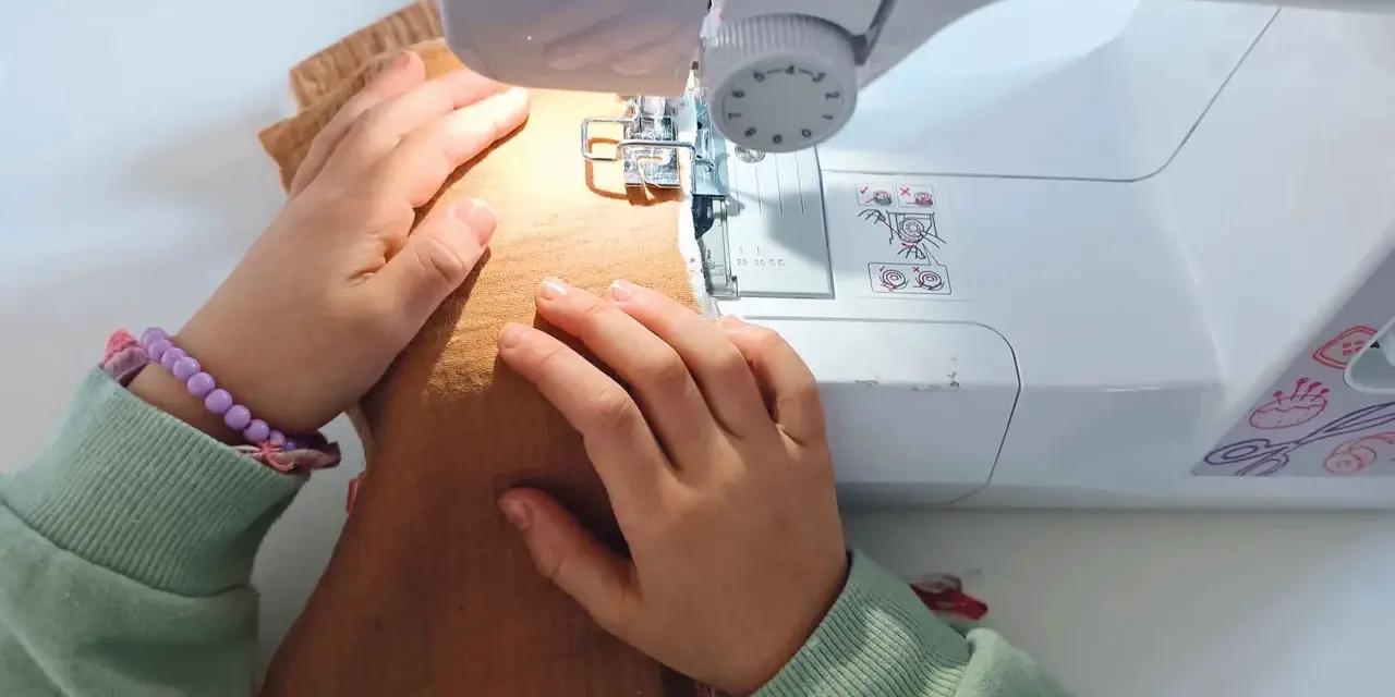 Mains d'enfant guidant un tissu sous une machine à coudre, apprenant comment coudre.