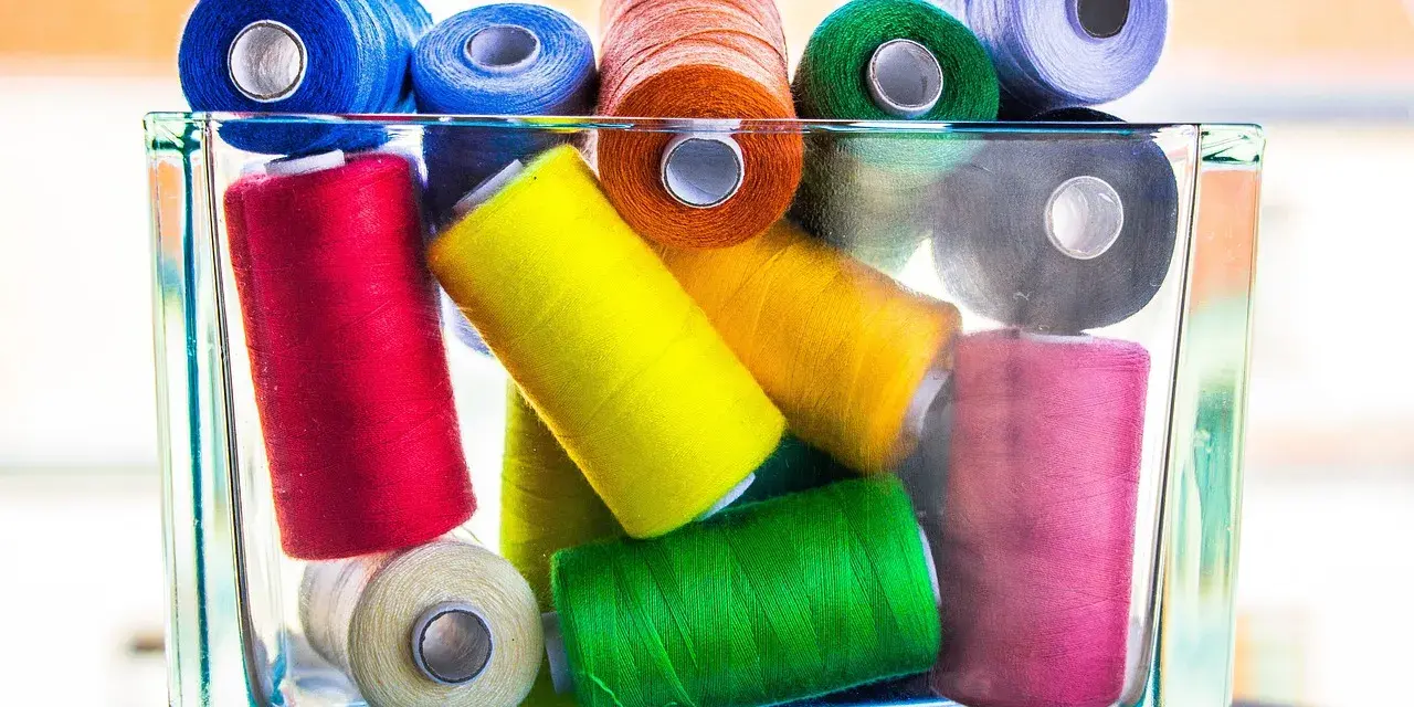 Un assortiment coloré de bobines de fil coton ou polyester, empilées dans un pot en verre.