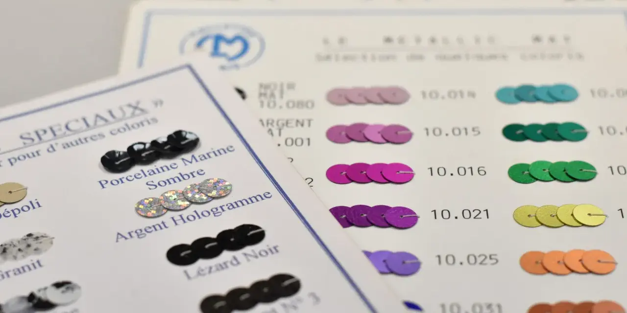 Échantillons de sequins pour faire un motif. Des sequins noirs, argentés, roses, violets, verts, jaunes et orangés sont présentés sur des fiches de couleurs.