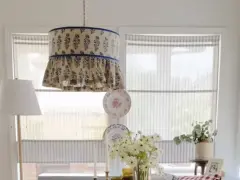 Un abat-jour suspendu avec un motif floral bleu et des volants, une excellente idée déco abat jour. Des assiettes décoratives et des fleurs complètent la scène.
