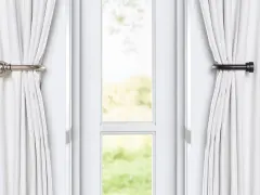 Rideaux blancs retenus par des embrasses métalliques, comme un nœud élégant, devant une fenêtre lumineuse.