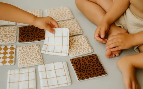 Petites mains d'enfant choisissant parmi des lingettes lavables bébé aux motifs variés : léopard, carreaux, et quadrillés. Idéal pour le change.