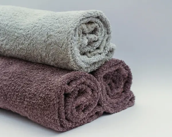 Trois serviettes de bain roulées, une grise et deux prune, prêtes à être cousues pour un projet de couture.