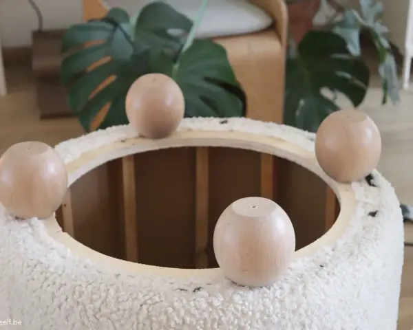 Quatre pieds ronds en bois sont posés sur le bord d'un pouf rond en tissu bouclette, prêt à recouvrir.