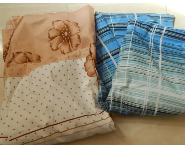 Tissus pliés, un à fleurs beiges et pois, l'autre à rayures bleues. Idéal pour apprendre comment faire un drap housse.