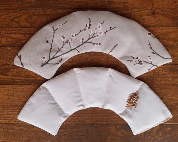 Tuto bouillotte sèche cervicale : deux coussins en tissu, l'un décoré de fleurs de cerisier, l'autre prêt à être rempli de grains.
