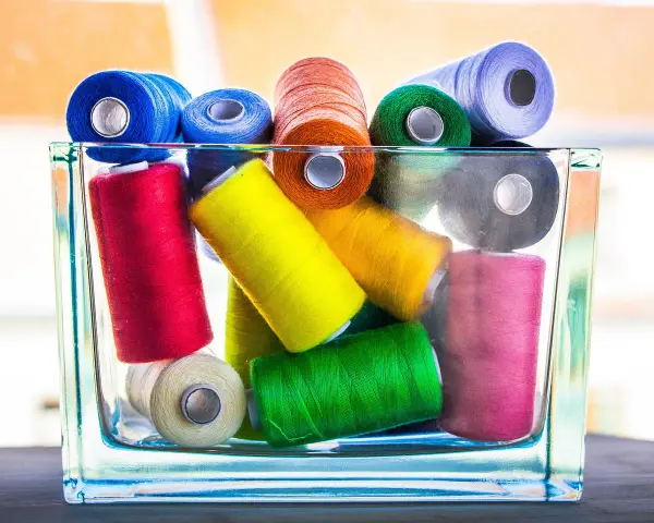 Un assortiment coloré de bobines de fil coton ou polyester, empilées dans un pot en verre.