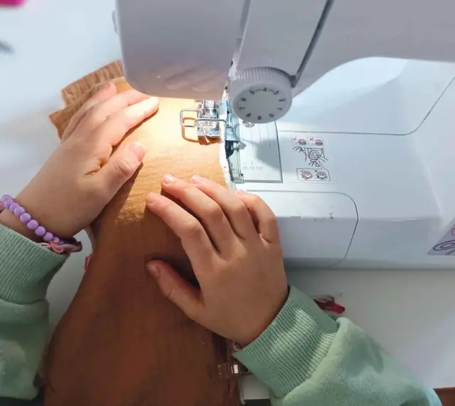 Mains d'enfant guidant un tissu sous une machine à coudre, apprenant comment coudre.