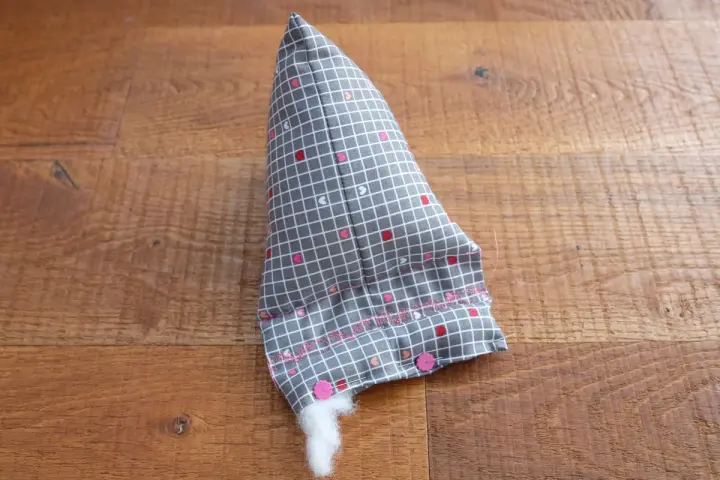 Un berlingot tissu gris à petits cœurs roses et blancs, en cours de rembourrage, est posé sur un parquet en bois.