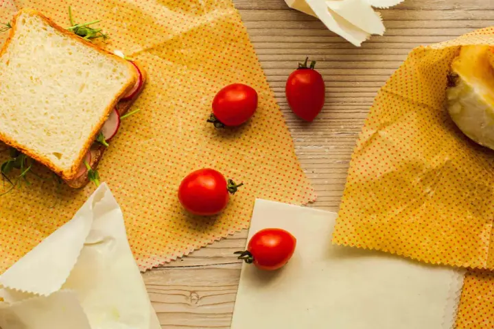 Un sandwich, des tomates et un morceau de fromage sont présentés sur des bee wraps maison à pois rouges sur fond de bois.