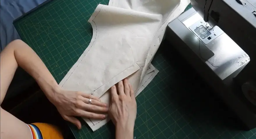Mains travaillant sur un patron de couture, ajustant un tissu pour une poche raglan, à côté d'une machine à coudre Singer.