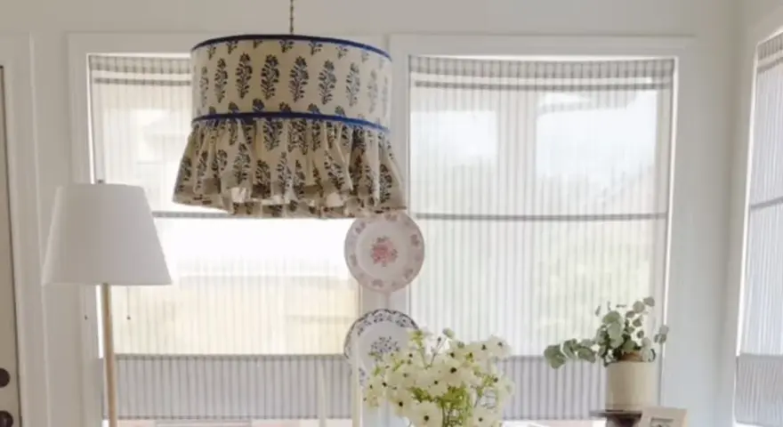 Un abat-jour suspendu avec un motif floral bleu et des volants, une excellente idée déco abat jour. Des assiettes décoratives et des fleurs complètent la scène.