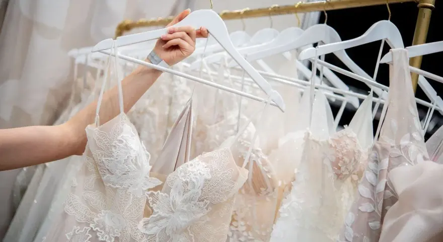 Une main choisit une robe de mariée, révélant la beauté des dentelles et des broderies. Quel tissu pour robe de mariée ? Ici, la délicatesse est reine.
