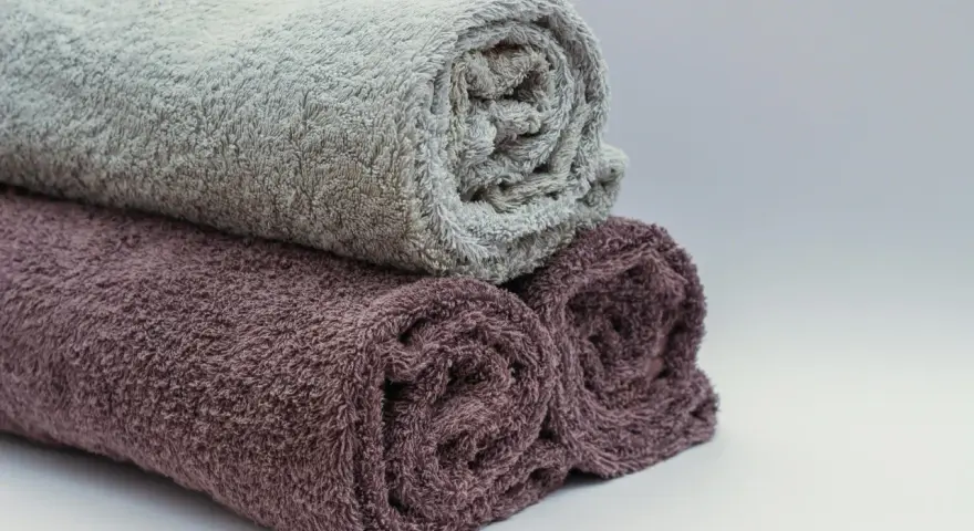 Trois serviettes de bain roulées, une grise et deux prune, prêtes à être cousues pour un projet de couture.