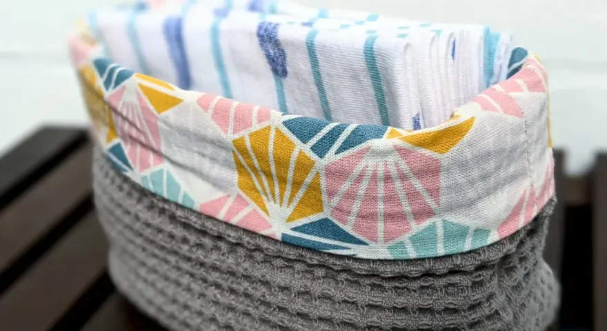 Un panier en tissu gris avec un motif géométrique coloré contient des mouchoirs en tissu. Une idée pour savoir que faire avec des mouchoirs en tissu.