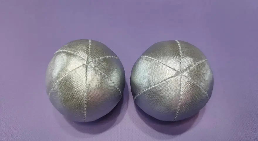 Deux balles en tissu argenté, parfaites pour un **patron gratuit balle en tissu**. Elles sont posées sur un fond violet.