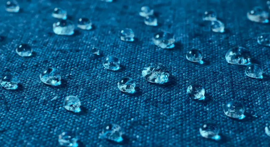 Gouttes d'eau perlant sur un tissu bleu, illustrant comment imperméabiliser un tissu naturellement.