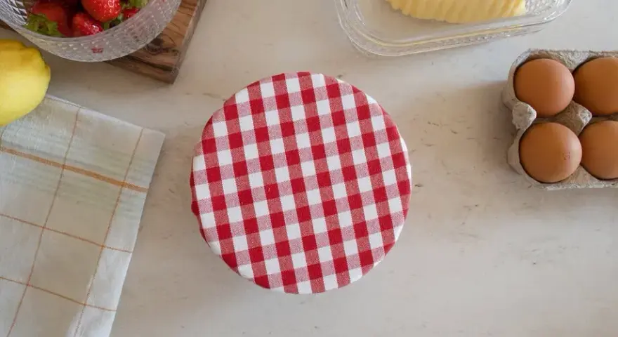 Préparation d'une charlotte alimentaire : fraises, citron, beurre, œufs et un couvercle à carreaux rouges et blancs.