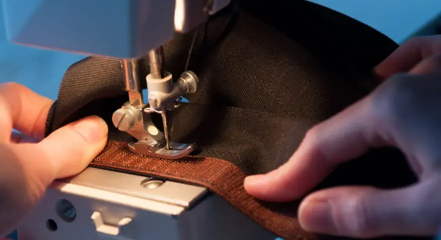 Mains habiles guidant un tissu noir sous une machine à coudre pour coudre du velcro marron.