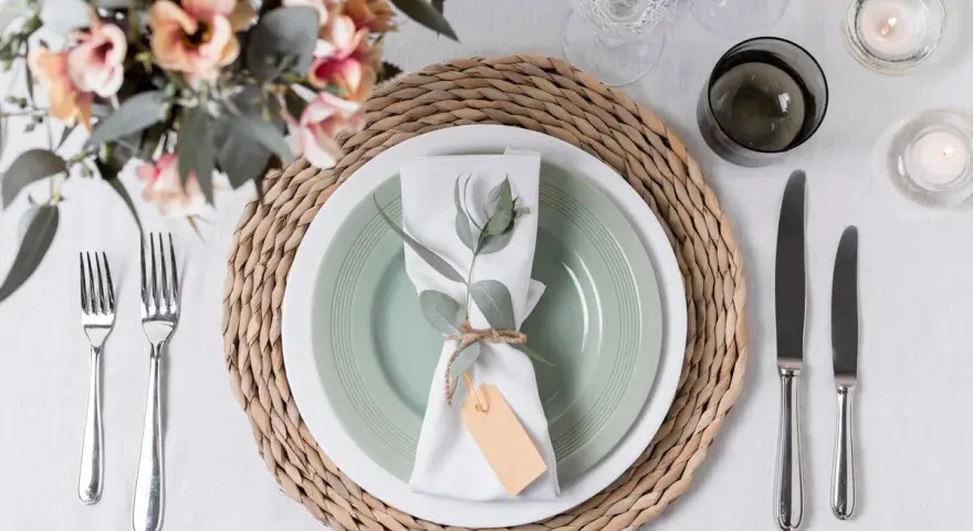 Une table dressée avec une assiette verte, une serviette blanche décorée d'une branche d'eucalyptus et d'une étiquette, le tout sur un rond de serviette fait maison.