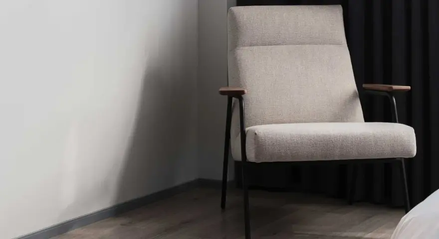 Fauteuil moderne avec un élégant tissu assise chaise, pieds fins et accoudoirs en bois. Il est placé près d'un mur blanc et de rideaux sombres.