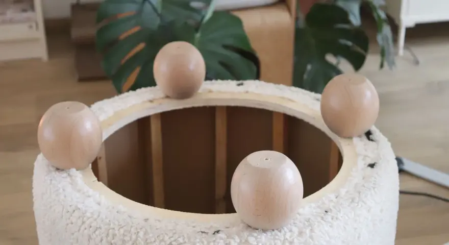 Quatre pieds ronds en bois sont posés sur le bord d'un pouf rond en tissu bouclette, prêt à recouvrir.