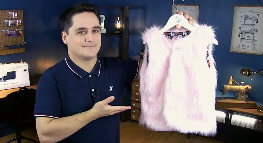 Un homme présente un adorable gilet berger bébé en fausse fourrure rose. Un patron gratuit pour le coudre est disponible.