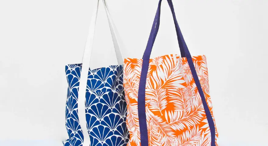 Deux sacs fourre-tout aux motifs vibrants : un bleu avec des éventails blancs, l'autre orange avec des feuilles de palmier blanches. Un patron de sac gratuit à télécharger pour créer vos propres accessoires.