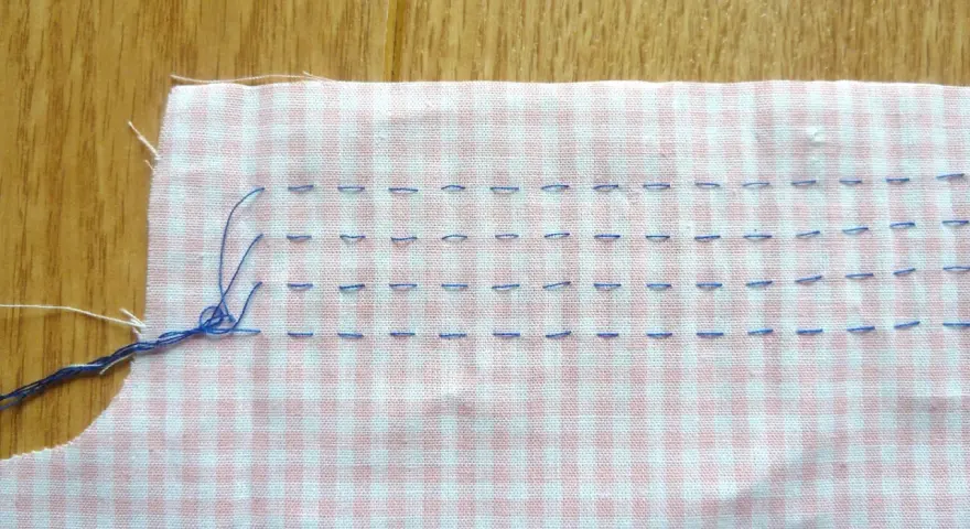 Tissu à carreaux rose et blanc avec des points de couture bleus, préparant un smock couture.
