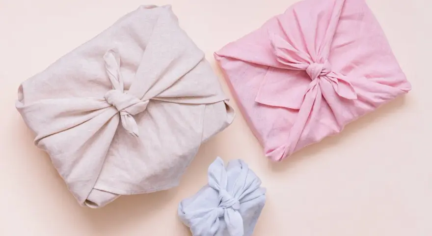 Trois paquets cadeaux joliment emballés dans des tissus de différentes couleurs (beige, rose, bleu clair). Lequel tissu pour furoshiki ? Le lin semble idéal.