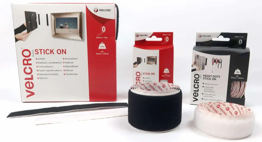 Comment poser du velcro adhésif : démonstration avec des rouleaux et boîtes de différentes tailles pour fixer cadres et outils.