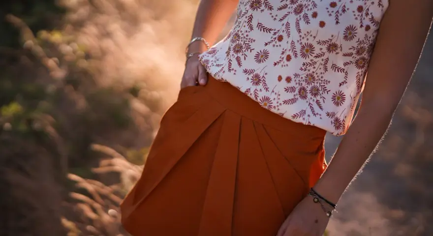 Jupe tulipe orange à plis, portée avec un haut fleuri. Le soleil couchant illumine la scène.