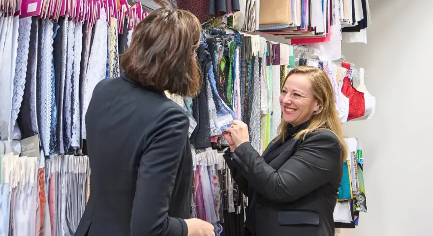 Deux femmes discutent devant un mur de tissus. L'une montre un échantillon de vêtement en fibre de bois à l'autre.