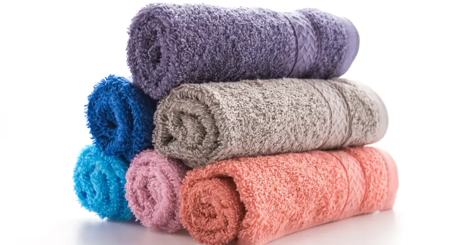 Pile de serviettes de bain roulées aux couleurs vives : violet, bleu, gris, rose et corail. La matière douce invite à la détente.
