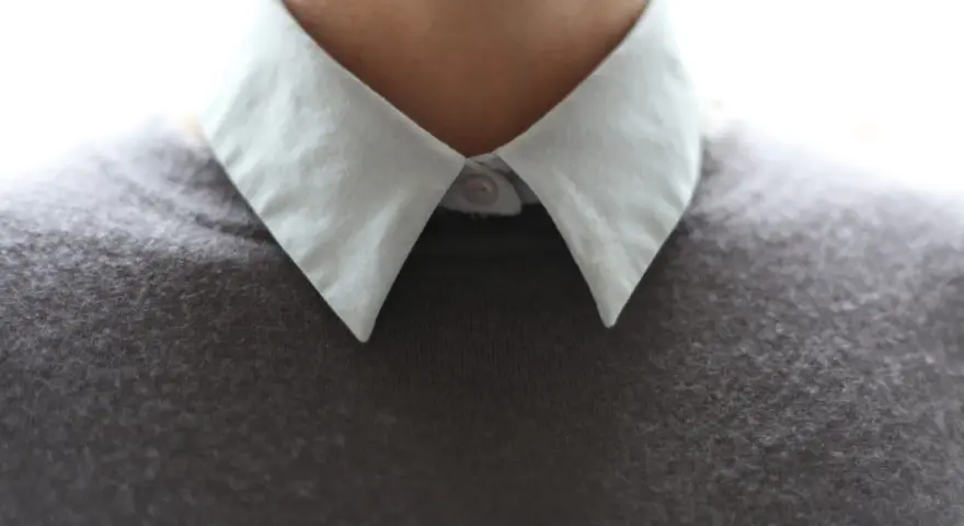 Gros plan sur un col froncé blanc sur un pull gris.