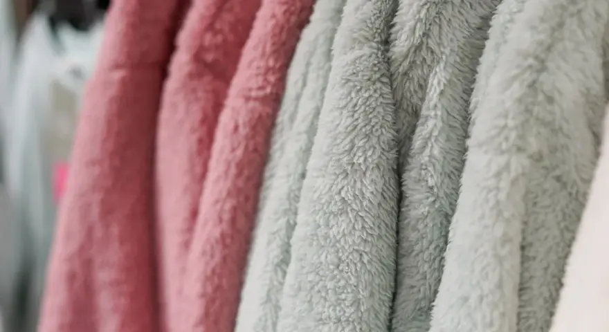 Des vêtements douillets en matière molleton, aux couleurs rose et vert d'eau, sont suspendus sur des cintres.
