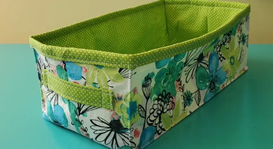 Panier rectangulaire en tissu, doublé de pois verts. Son extérieur est orné d'un motif floral coloré, parfait pour ranger vos affaires avec style.