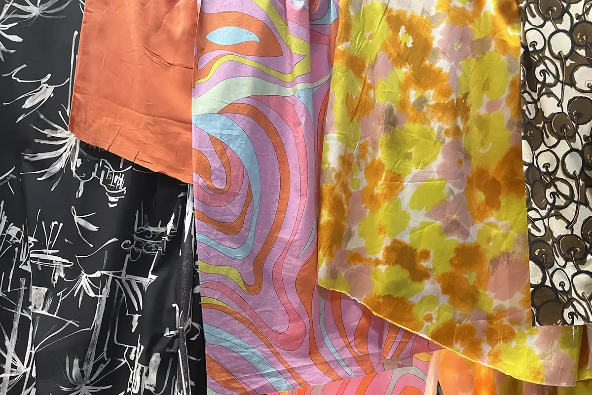 Échantillons de tissus aux motifs variés : abstrait noir et blanc, orange uni, psychédélique rose et bleu, floral jaune et orange, et cerises marron.