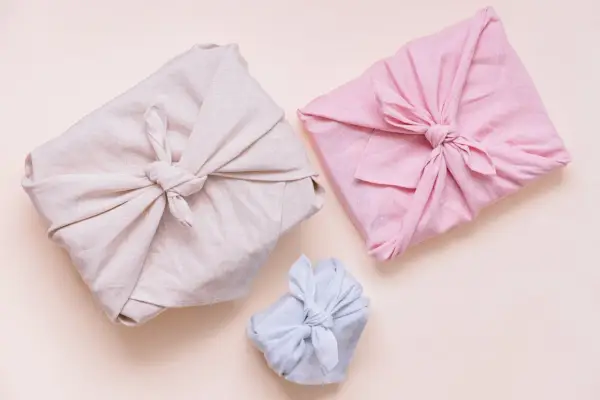 Trois paquets cadeaux joliment emballés dans des tissus de différentes couleurs (beige, rose, bleu clair). Lequel tissu pour furoshiki ? Le lin semble idéal.