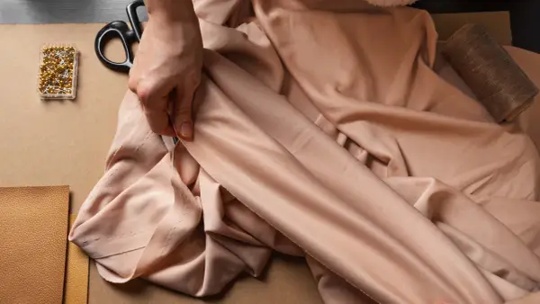 Mains tenant un tissu drapé, avec des épingles, des ciseaux et du fil. La viscose, c'est quoi ? Une matière douce et fluide pour la couture.