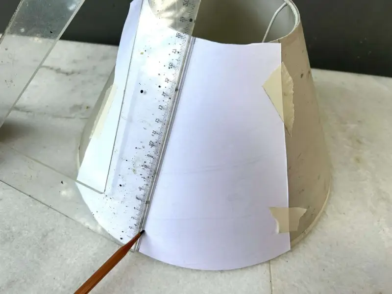 Un crayon et une règle mesurent un gabarit en papier pour un abat-jour DIY.