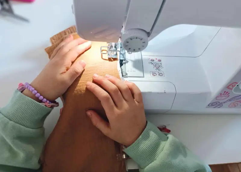 Mains d'enfant guidant un tissu sous une machine à coudre, apprenant comment coudre.